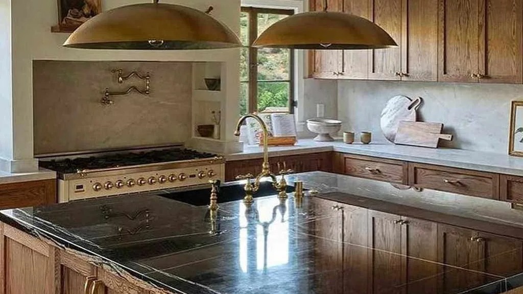 A cozinha da casa de Sabrina Carpenter apresenta ilha de mármore preto, armários de carvalho e fogão italiano Ilve Cozinha com ilha de mármore preto, pia, torneira dourada, fogão Ilve creme e armários de madeira