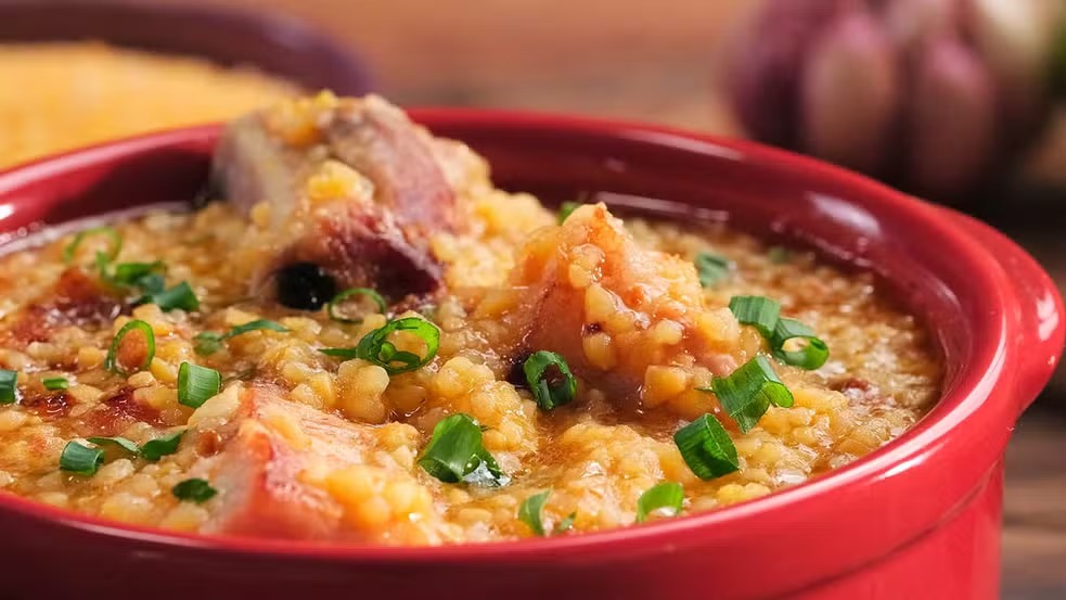 Canjiquinha com costelinha suína: uma refeição quentinha e saborosa para aquecer seu dia. Close-up de canjiquinha com costelinha suína em tigela vermelha, guarnecida com cebolinha verde picada