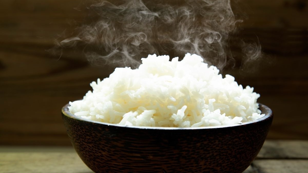 Arroz soltinho e fumegante: siga as dicas para preparar o acompanhamento perfeito que não gruda. Tigela de madeira com arroz branco cozido e fumegante sobre superfície de madeira.