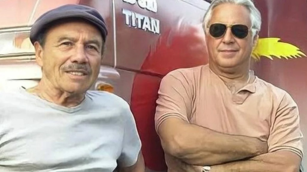 Antonio Fagundes de boné e Stênio Garcia de óculos escuros sorriem ao lado de caminhão vermelho escrito Titan.