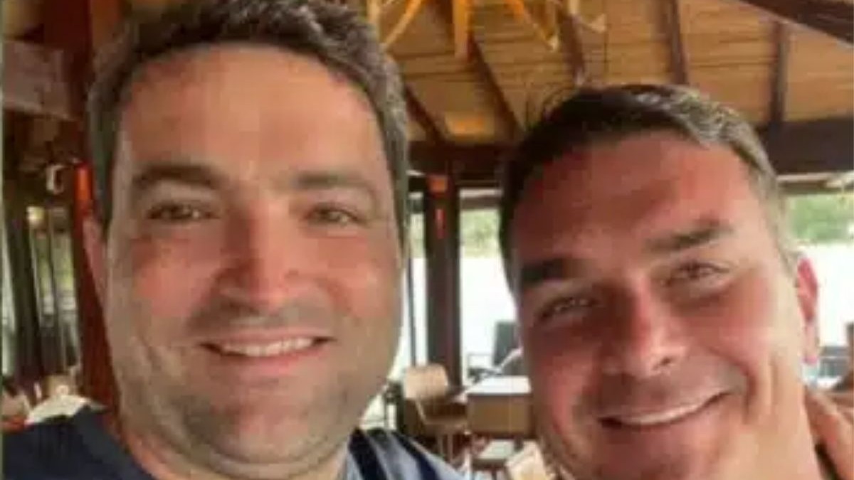 Flávio Bolsonaro (à direita) e Willer Tomaz, pivô da disputa judicial por mansão em Angra dos Reis. Dois homens sorrindo para a câmera, um deles Flávio Bolsonaro, em um ambiente interno.
