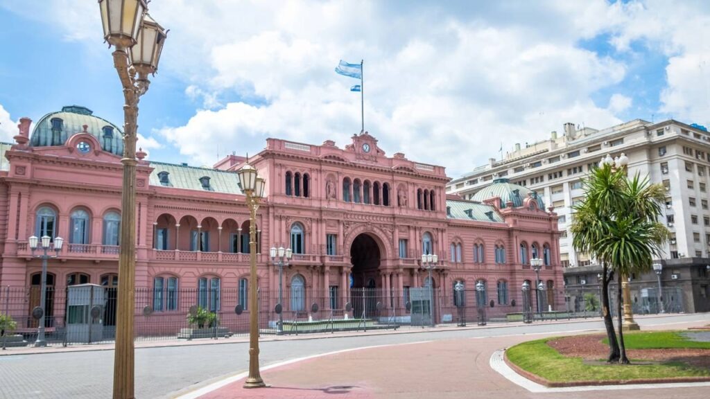 A Casa Rosada, sede do governo argentino, é o cenário das decisões que moldam a Previdência Social e mobilizam protestos. Casa Rosada, palácio presidencial da Argentina, com bandeiras hasteadas, em dia nublado