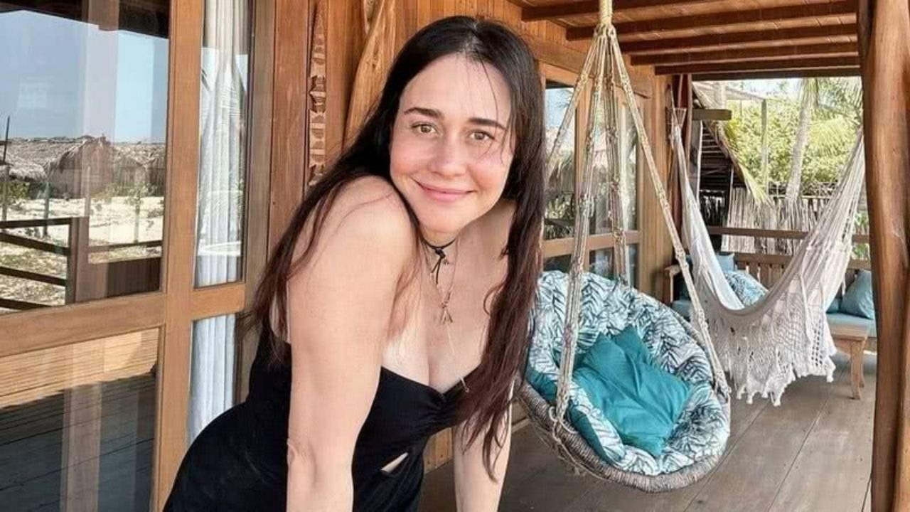 Alessandra Negrini prepara seu retorno às telinhas como um dos nomes centrais da próxima novela das sete da TV Globo. Foto: Reprodução Alessandra Negrini sorrindo em um terraço de madeira com cadeiras suspensas e vista tropical