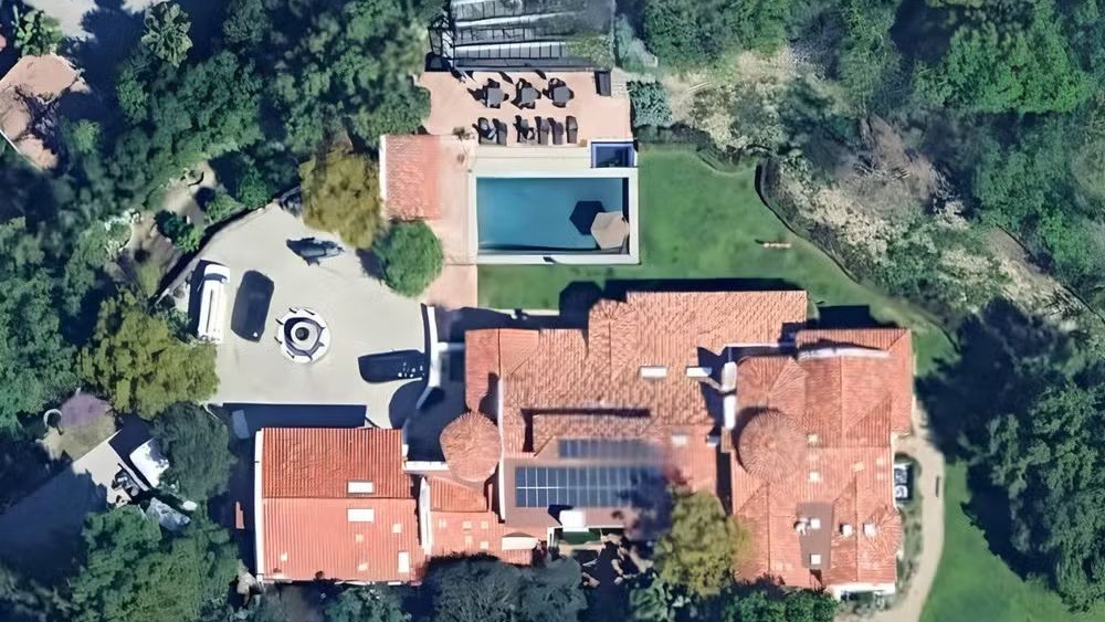 Vista aérea de uma das luxuosas residências dos artistas do Rock in Rio 2026, onde buscam privacidade e descanso entre turnês Vista aérea de propriedade luxuosa com telhados de telha, piscina, carros na entrada e painéis solares