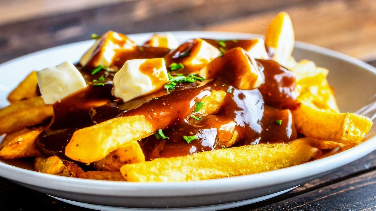 Poutine em um prato branco, com batatas fritas, queijo coalho, molho gravy e salsa.