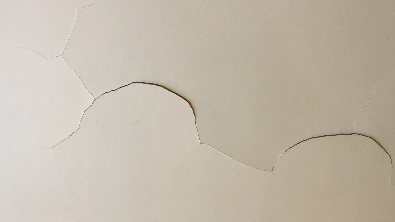 O descascamento e as rachaduras na pintura são sinais comuns de umidade, problema que pode ser resolvido com as dicas de reparo doméstico. Pintura clara descascando e rachada em uma parede, mostrando danos por umidade
