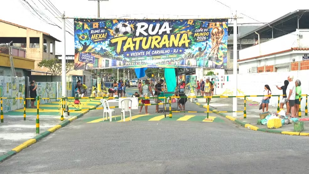 A Rua Taturana, em Vicente de Carvalho, decorada pela comunidade para o concurso da Copa do Mundo 2026, que a consagrou vencedora. Rua Taturana com faixas verde e amarela, pessoas e banner da Copa do Mundo 2026.