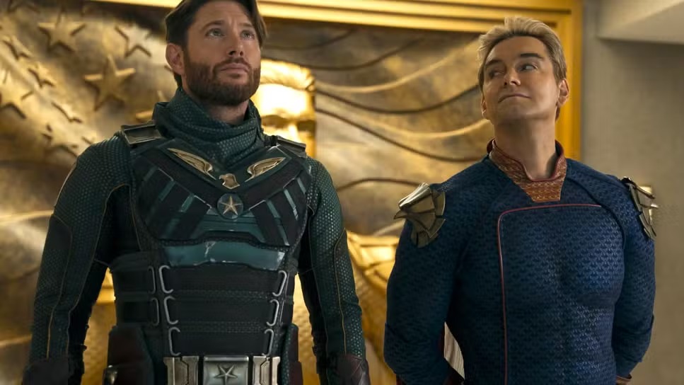 Capitão Pátria e Soldier Boy em The Boys, série do Prime Video que se prepara para seu aguardado e violento desfecho. Jensen Ackles (Soldier Boy) e Antony Starr (Capitão Pátria) em uniformes de super-heróis, olhando para cima.
