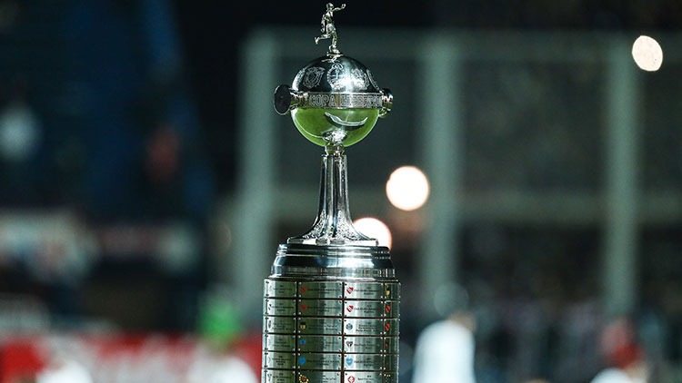A taça da Copa Libertadores, o objeto de desejo dos clubes sul-americanos, em destaque após o sorteio dos confrontos das oitavas de final. Foto: Divulgação A icônica taça prateada da Copa Libertadores em destaque, com fundo escuro e desfocado.