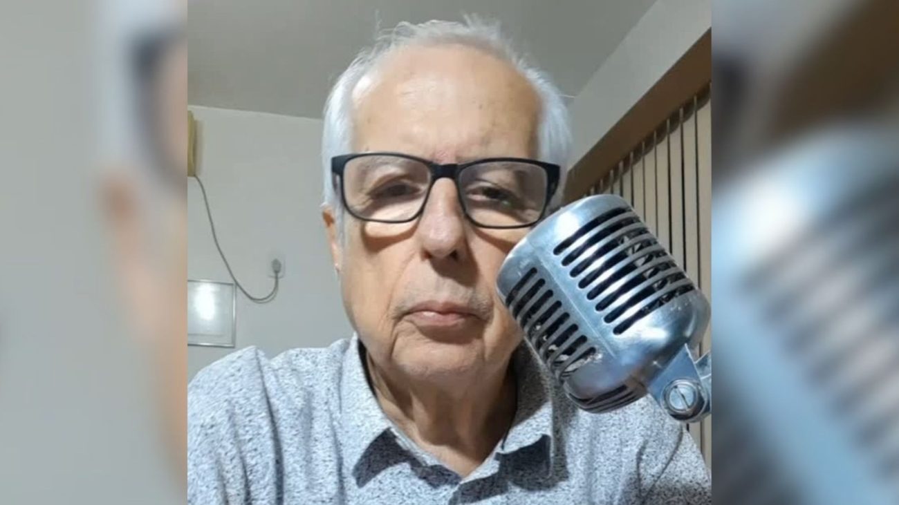 Ubirajara Garcia, o Bira, uma das vozes mais marcantes do rádio do Sul de Santa Catarina, em registro com seu microfone. Foto: Reprodução Homem idoso com óculos e cabelos brancos segurando um microfone vintage prateado