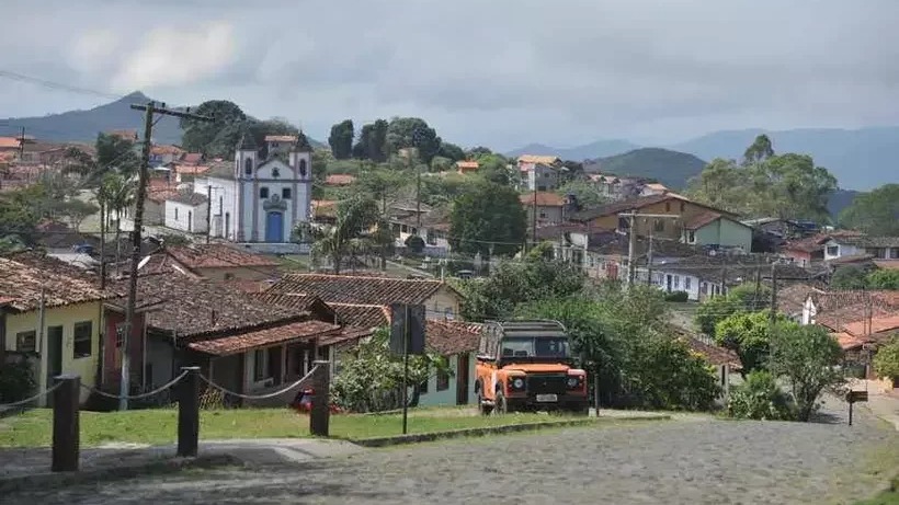 Cidade histórica com igreja colonial branca e azul, casas telhadas e jipe laranja.