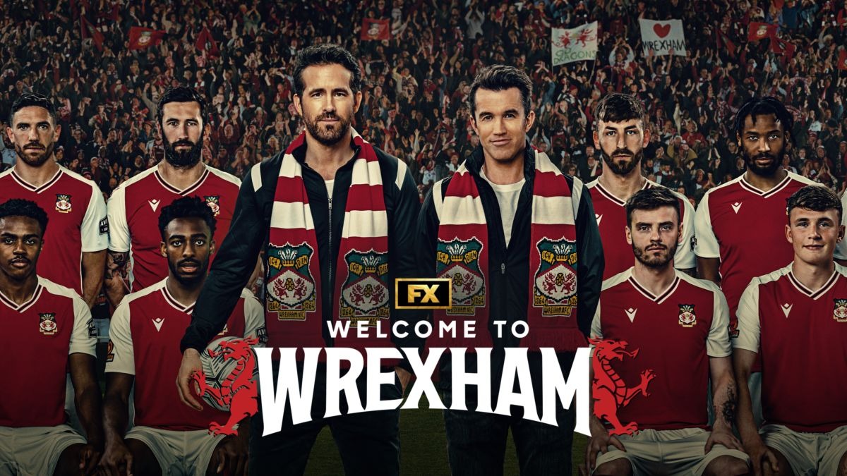 A paixão pelo futebol e a gestão do Wrexham AFC são o foco da série "Bem-vindos a Wrexham", com Ryan Reynolds e Rob McElhenney. Ryan Reynolds e Rob McElhenney com jogadores do Wrexham. Título "Welcome to Wrexham" visível.