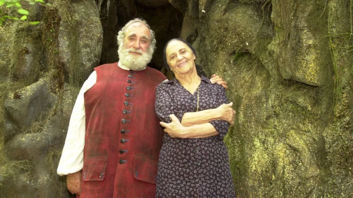 Atriz Laura Cardoso (&agrave; direita) e ator idoso sorriem, abra&ccedil;ados, em cen&aacute;rio rochoso com vegeta&ccedil;&atilde;o
