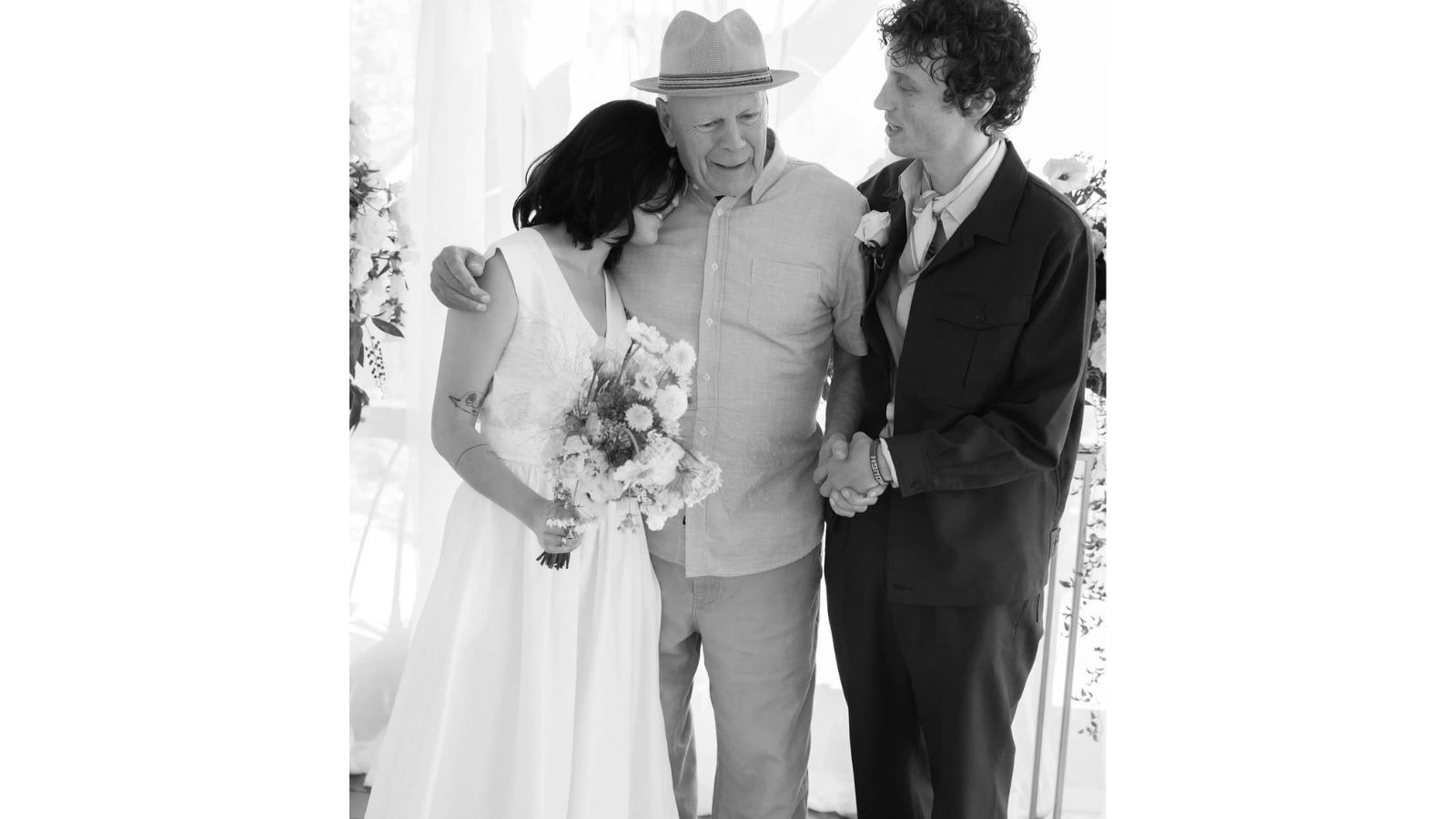 Bruce Willis sorri no casamento da filha Tallulah com Justin Acee, celebrando o momento familiar Bruce Willis, de chapéu, abraça a filha noiva com buquê e dá a mão ao genro