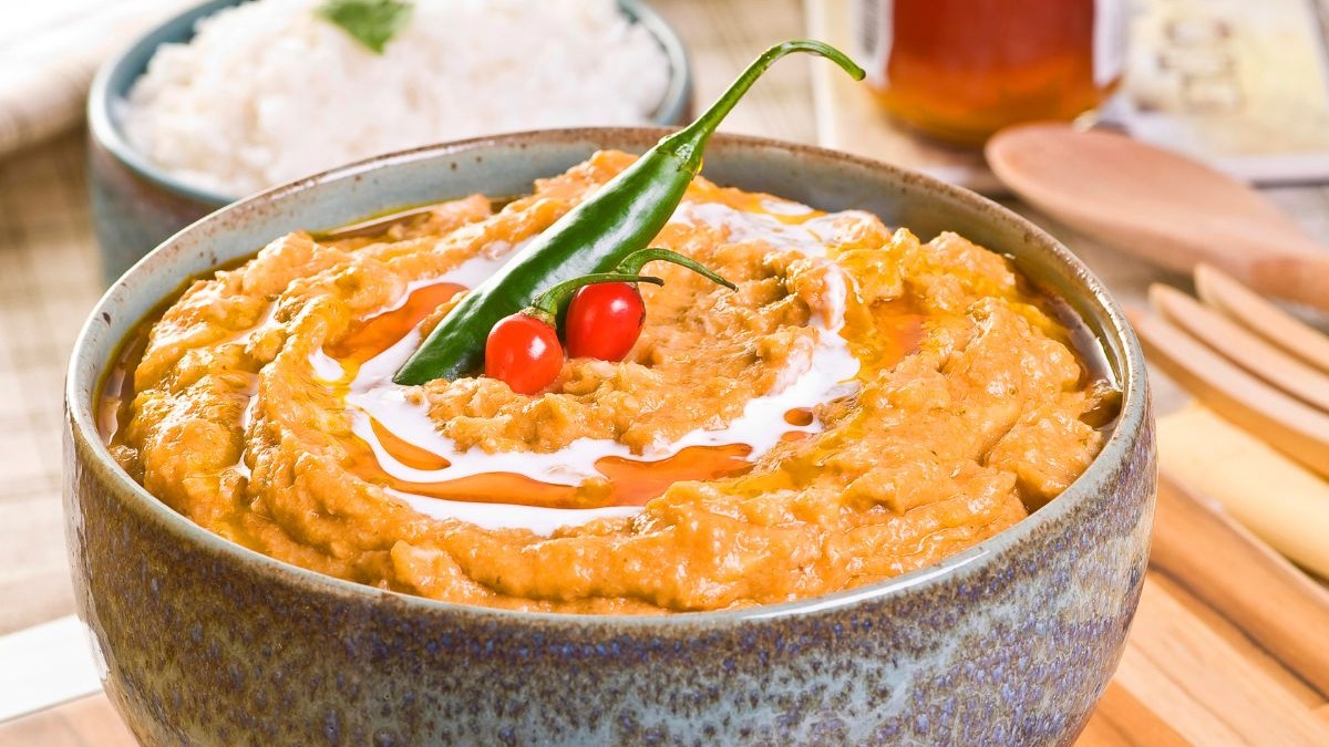 O vatapá, com sua textura aveludada, é um dos pratos baianos que confortam e aquecem nos dias mais frescos. Prato de vatapá cremoso com pimenta verde, duas pimentas vermelhas e arroz em tigela.