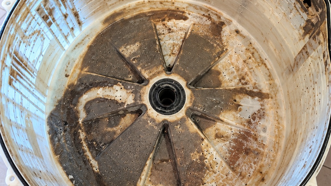 Máquinas de lavar acumulam sujeira, mofos e resíduos no tambor, exigindo limpeza periódica para garantir a higiene das roupas Interior de tambor de máquina de lavar em close-up, com sujeira escura de mofo e resíduos