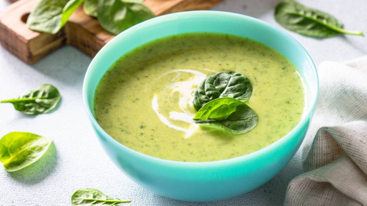 Aprenda a fazer a sopa cremosa de espinafre, rica em nutrientes e ideal para o inverno. Tigela turquesa com sopa cremosa de espinafre, decorada com folhas frescas e creme