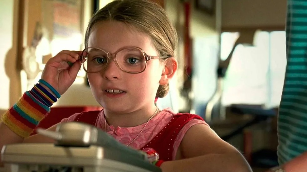 Em dias de frio, uma seleção de filmes promete aquecer os corações em sessões aconchegantes. Menina com óculos grandes e punhos coloridos ajusta as lentes, olhando para baixo.