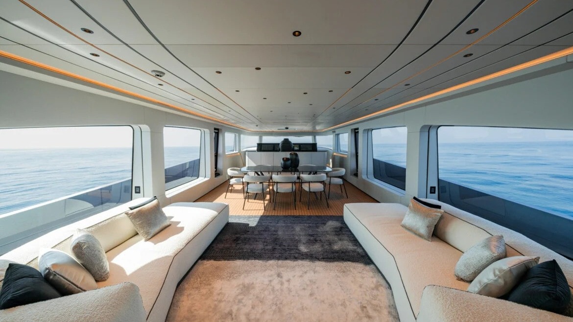 Luxuoso interior do superiate AB110 da Brabus, revelando a área social e sala de jantar do convés principal Interior de iate luxuoso com sofás brancos, mesa de jantar, janelas grandes e vista do oceano