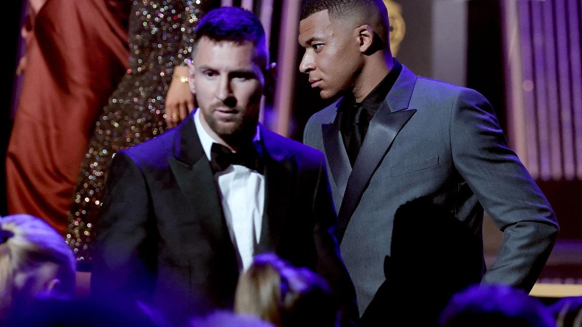 Lionel Messi e Kylian Mbappé, os principais concorrentes ao recorde de artilharia em Copas, reunidos em cerimônia. Lionel Messi de terno preto, Kylian Mbappé de terno cinza, olha para Messi, em evento formal.