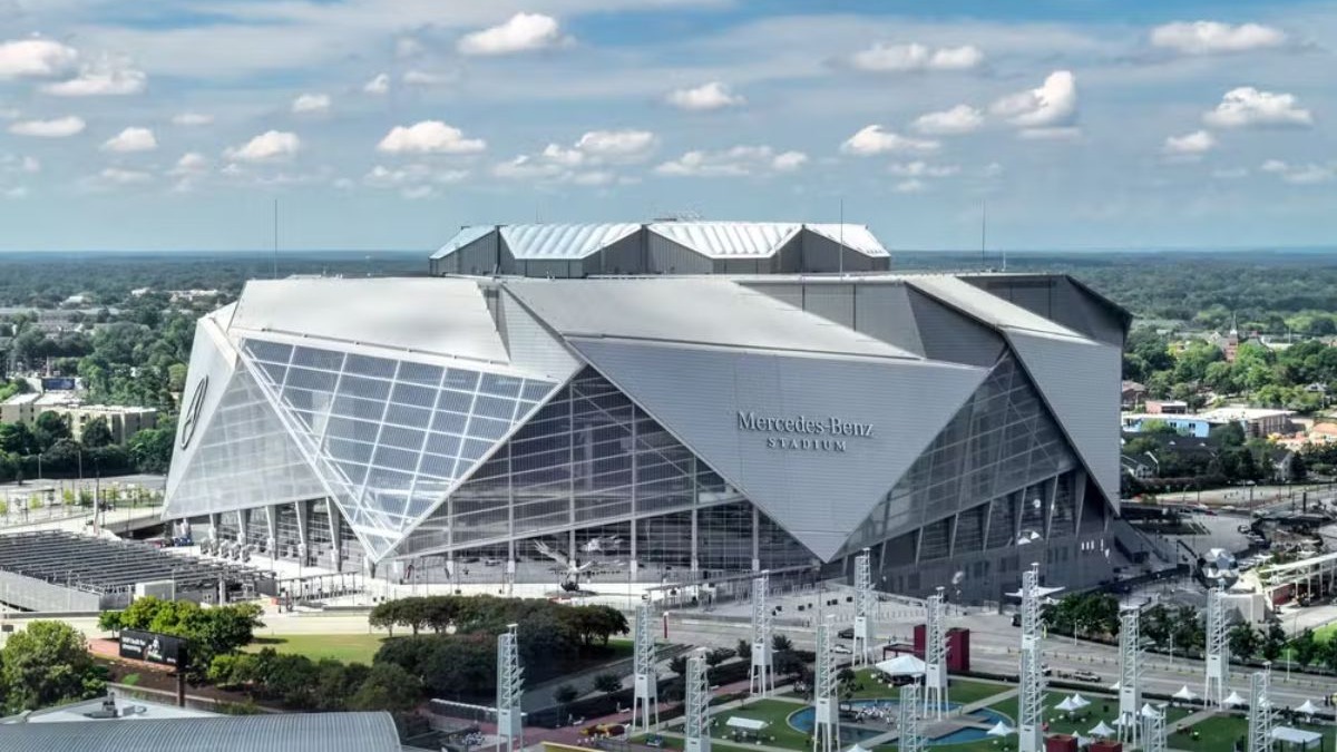Estádio Mercedes-Benz, em Atlanta Vista aérea do Mercedes-Benz Stadium, moderno e angular, com letreiro, rodeado por vegetação e prédios.