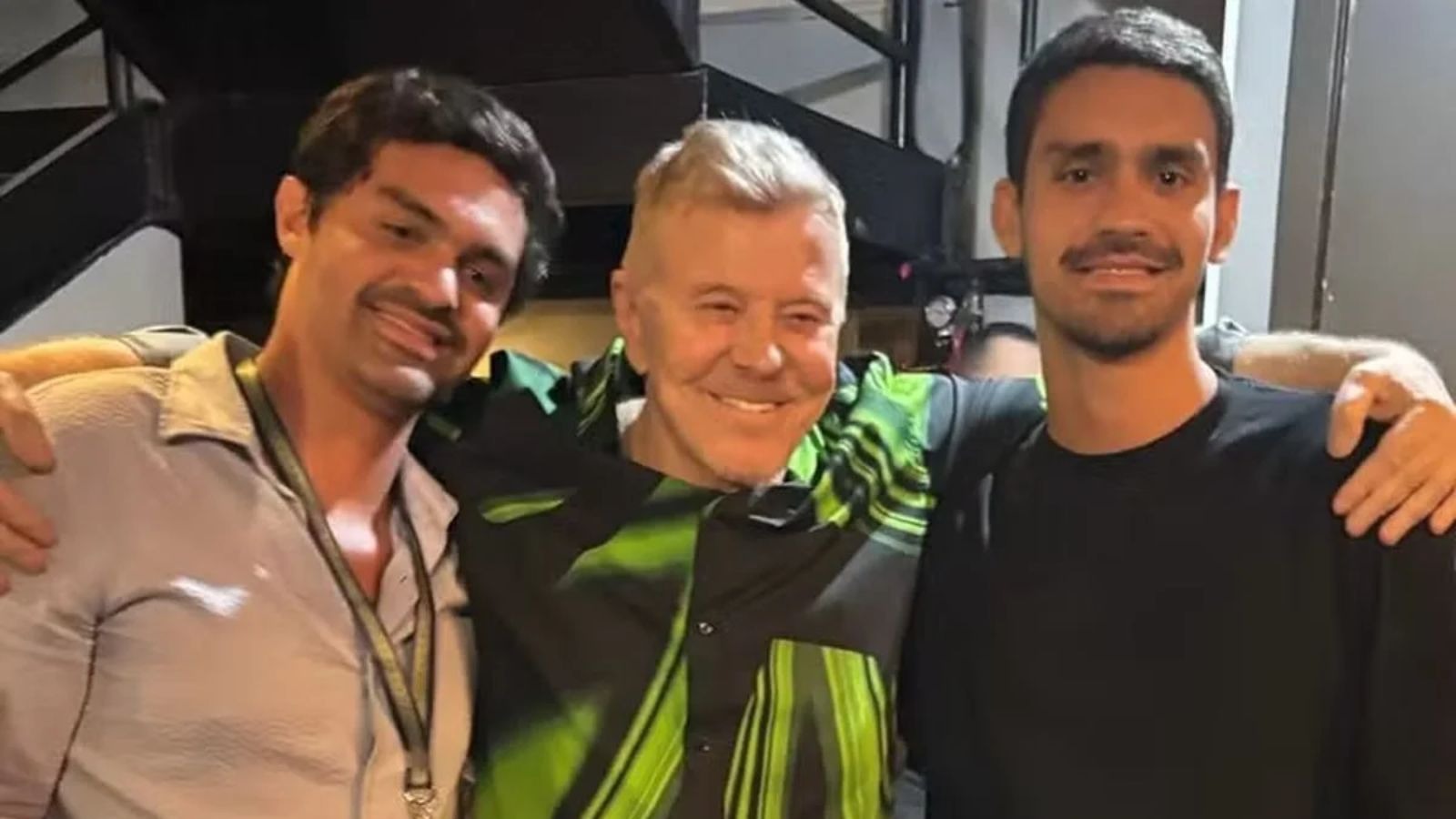 Miguel Falabella sorrindo, ladeado por dois homens com bra&ccedil;os nos ombros