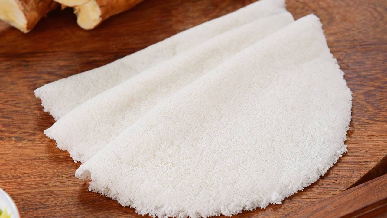 Tapiocas são uma opção energética e sem glúten para o café da manhã, como sugerido para a quarta-feira no plano alimentar. Três tapiocas brancas dobradas em um balcão de madeira com mandiocas ao fundo