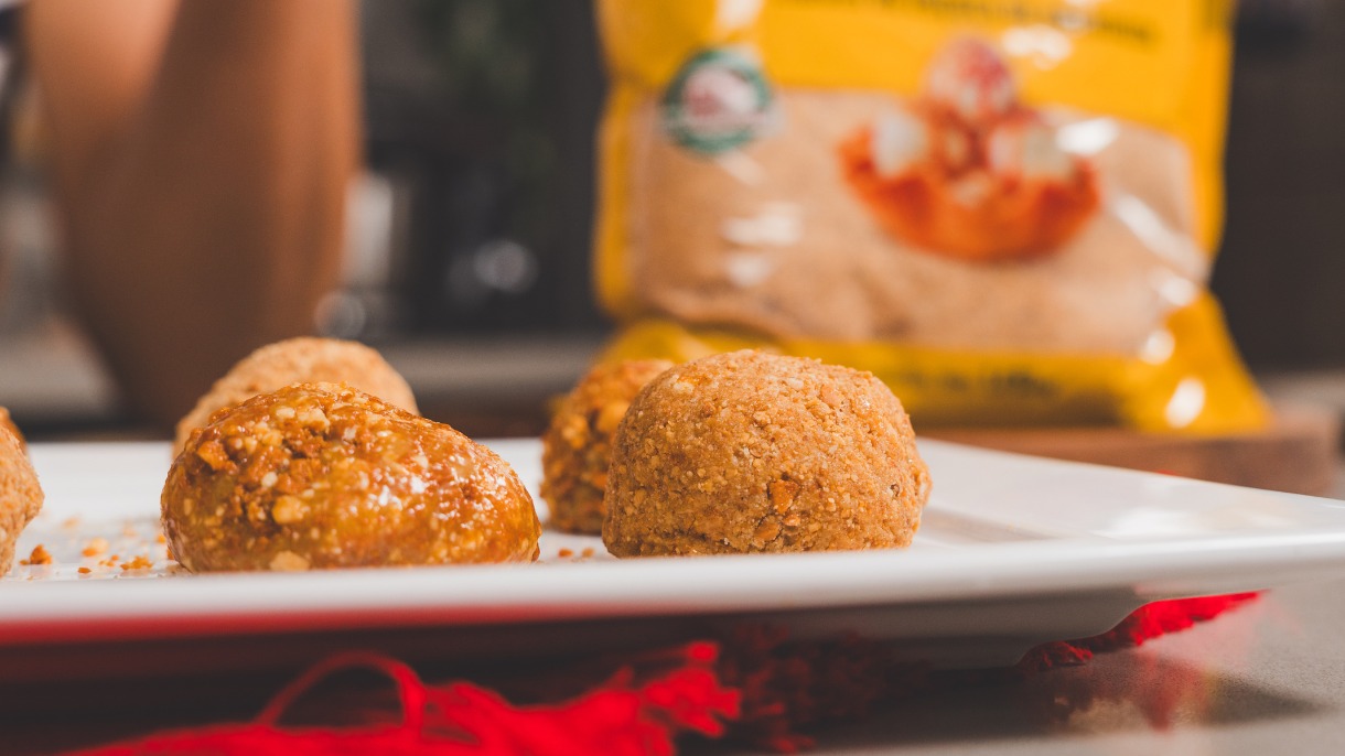 Brigadeiros crocantes de amendoim em prato branco, com saco amarelo desfocado ao fundo