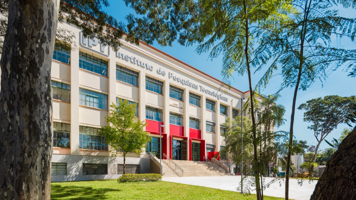 Fachada do edif&iacute;cio IPT com logo Google na entrada, gramado e &aacute;rvores sob c&eacute;u azul.