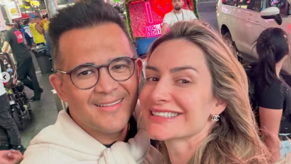 Empresário Bruno Avelar, uma das vítimas do acidente aéreo, em registro ao lado de sua esposa. Homem de óculos e mulher sorrindo em selfie, fundo urbano noturno com letreiro 'NEW'