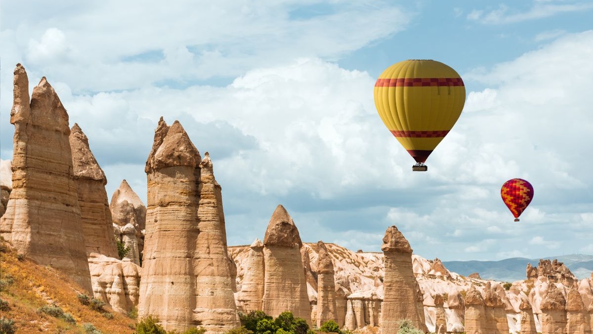 A Capadócia, na Turquia, é um dos destinos que se tornam mais acessíveis para brasileiros com a valorização do real. Dois balões de ar quente sobre formações rochosas (chaminés de fada) sob céu nublado.