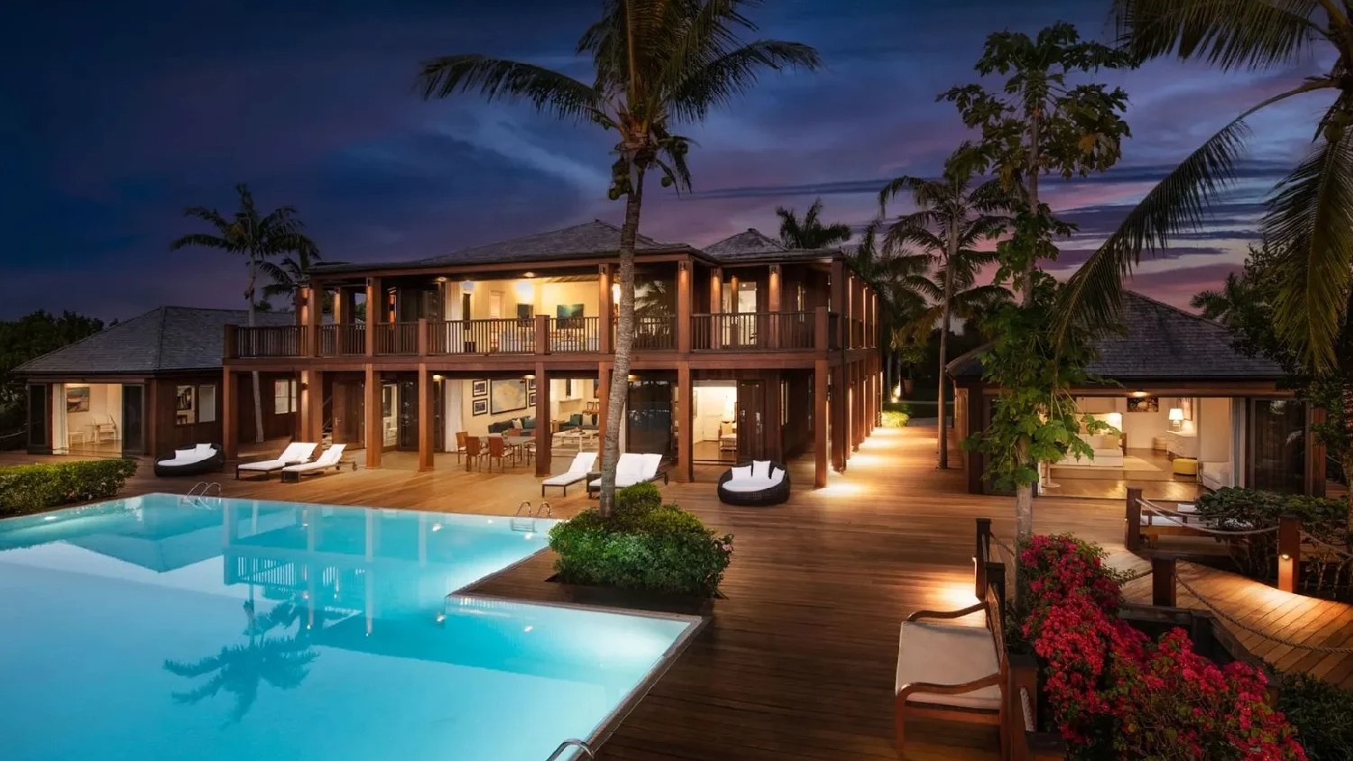 Uma das quatro piscinas da exclusiva propriedade de Bruce Willis em Parrot Cay, nas Ilhas Turcas e Caicos Luxuosa casa de madeira com piscina azul iluminada, deck de madeira e palmeiras à noite