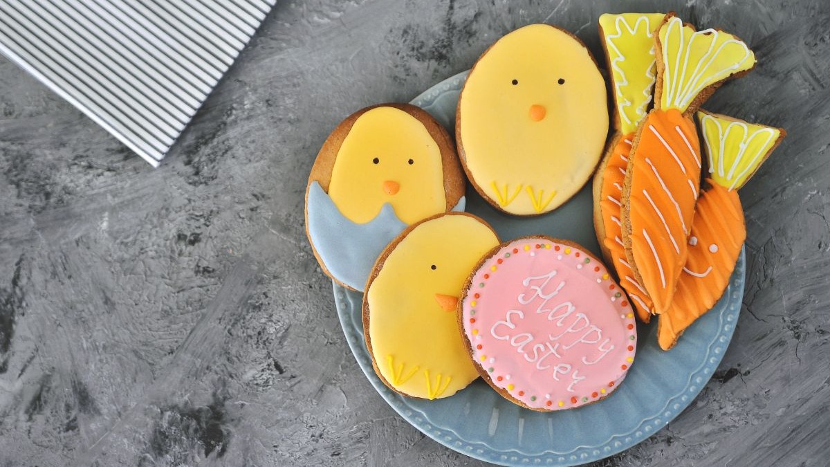 Biscoitos de P&aacute;scoa decorados em formato de pintinhos, ovos e cenouras, em um prato azul.