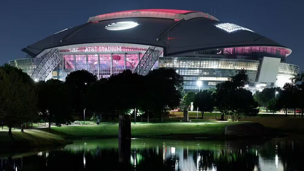 O AT&T Stadium, no Texas, um dos estádios modernos e com teto retrátil Estádio AT&T iluminado à noite, com luzes vermelhas e brancas, refletido em lago.