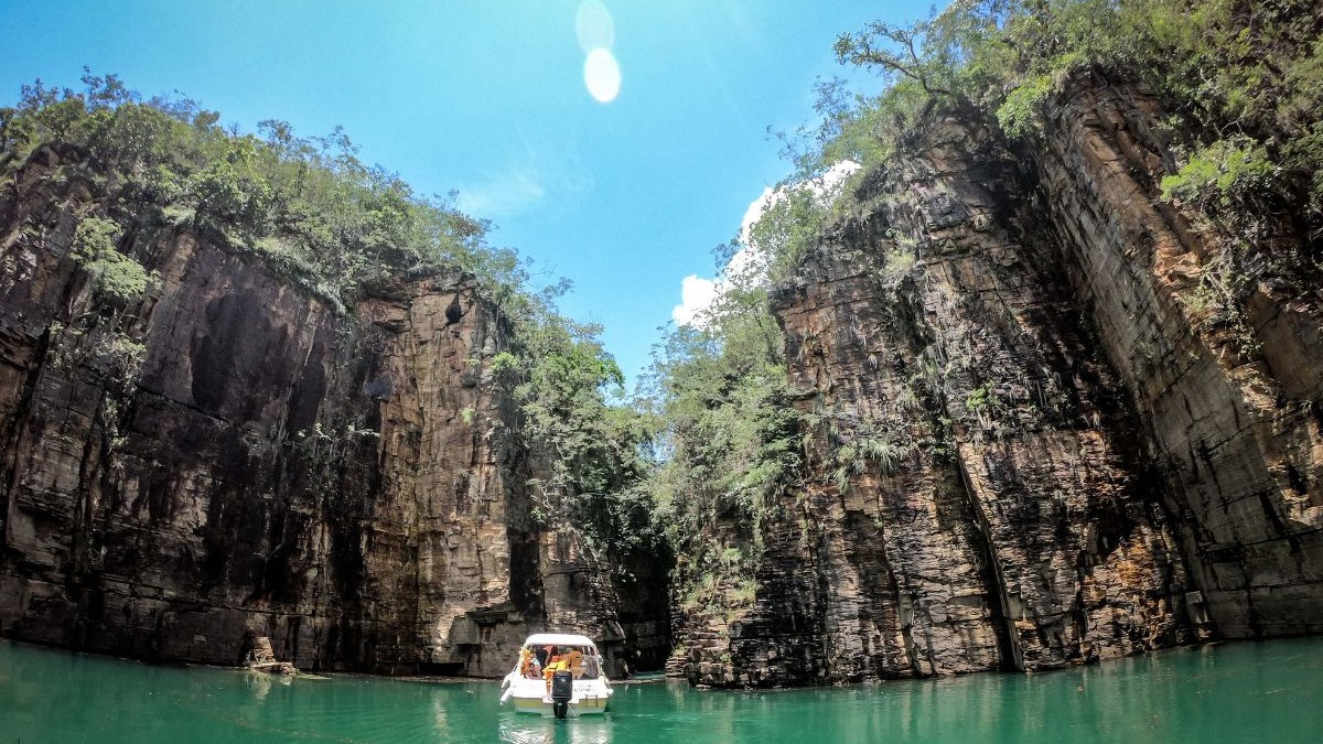 Barco em &aacute;gua verde cercado por altos c&acirc;nions rochosos sob c&eacute;u azul claro.