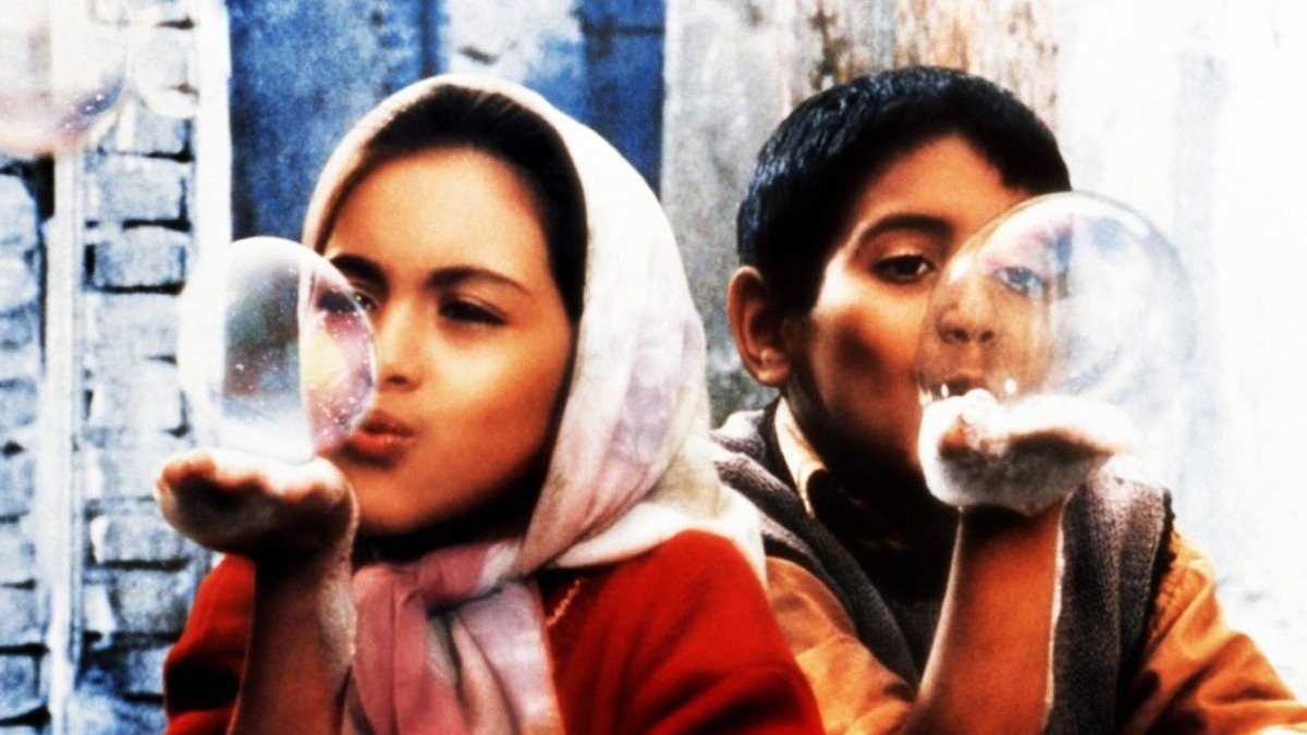 Duas crian&ccedil;as, uma menina de len&ccedil;o e um menino, sopram bolhas de sab&atilde;o.