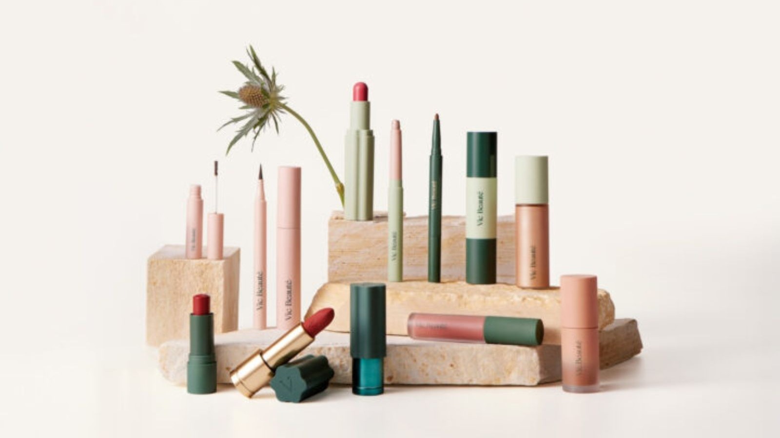Cole&ccedil;&atilde;o de maquiagens Vic Beaut&eacute; em tons de rosa, verde e vermelho, dispostas sobre blocos de pedra