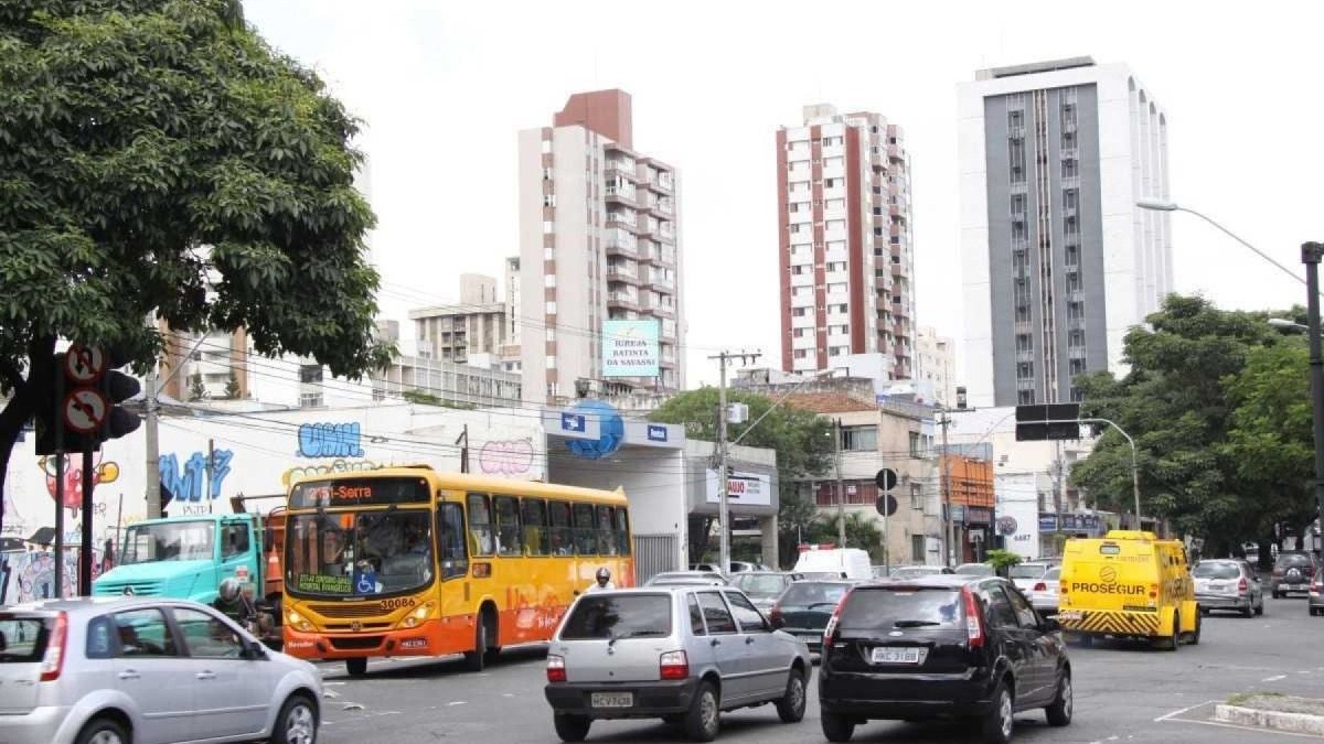 Ruas de Belo Horizonte, palco da história e do cotidiano, mantêm seu ritmo urbano e testemunham o legado dos nomes que as batizam. Rua movimentada de Belo Horizonte com ônibus amarelo, carros, caminhão, prédio alto e árvores.