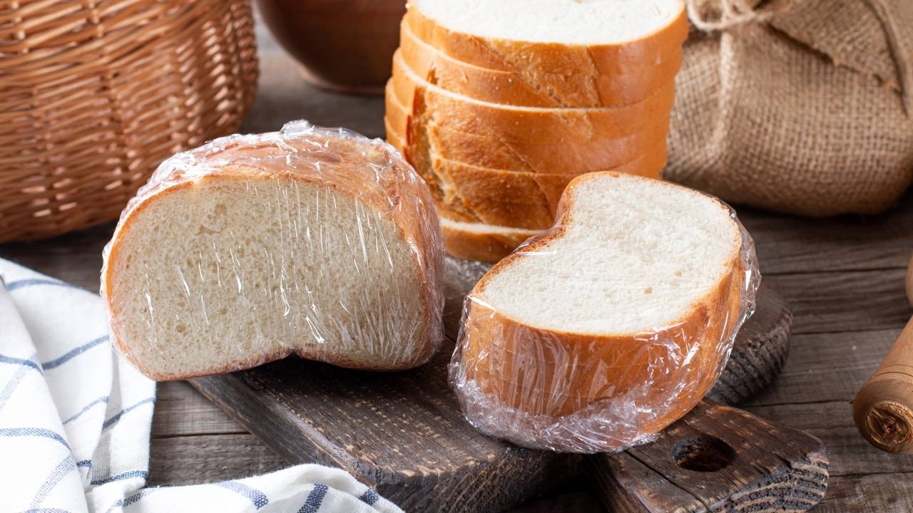 O hábito de congelar pão, como mostram as fatias embaladas, transforma seu amido e traz benefícios à saúde. Dois pedaços de pão embalados em plástico sobre tábua de madeira com pão fatiado