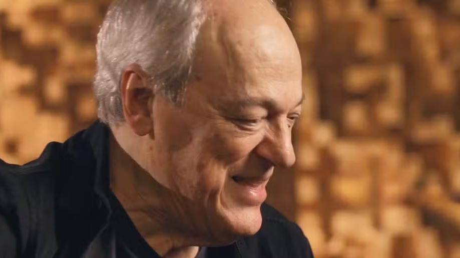 Toquinho apresenta a turnê "Só Tenho Tempo Pra Ser Feliz" no Vivo Rio, celebrando seus 80 anos. Foto: Reprodução / Vídeo Close-up de homem idoso sorrindo, com cabelo grisalho e roupa preta sobre fundo borrado