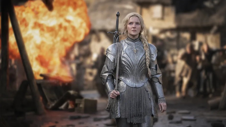 A segunda temporada de "O Senhor dos Anéis: Os Anéis de Poder" promete batalhas ainda mais grandiosas e um aprofundamento na Terra-média. Mulher de armadura prateada com espada nas costas em cena de batalha com explosão.