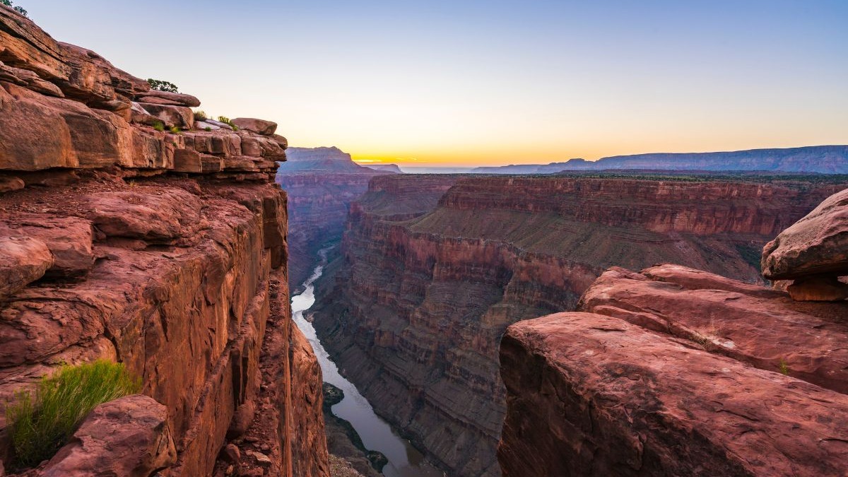 Vasta paisagem do Grand Canyon com um rio serpenteando por entre as imponentes rochas avermelhadas.