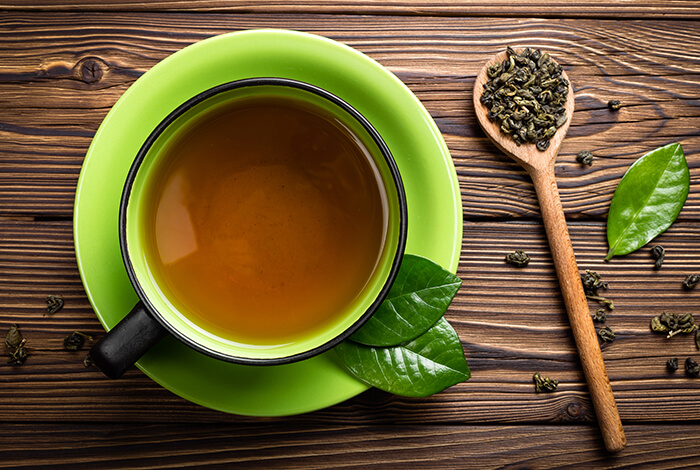 A cup of green tea with tea leaves next to it.