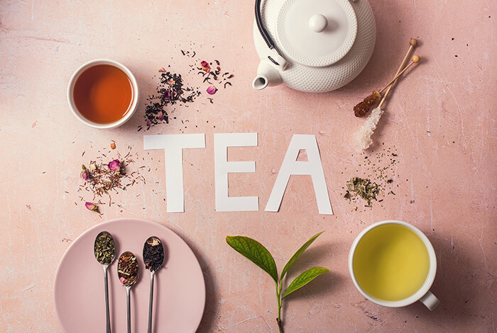 A pot of tea, a cup of green tea, 3 spoons full of herbal tea, and a cup of black tea.