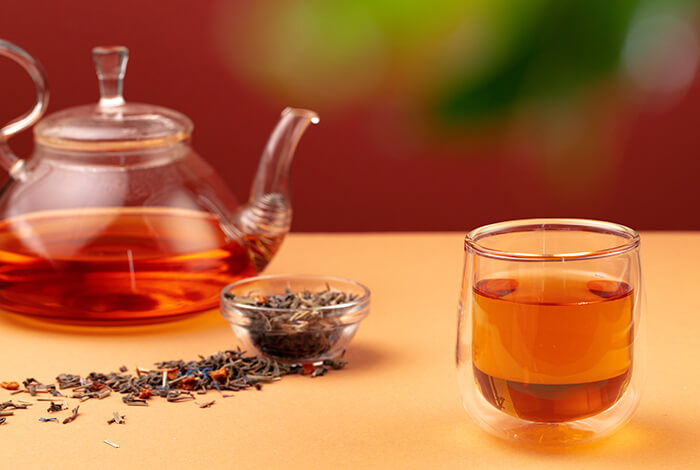 A glass pot, a cup of tea, and a bowl of herbs in the middle.
