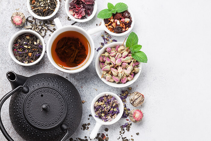 A cup of tea with a teapot and different herbs around it.