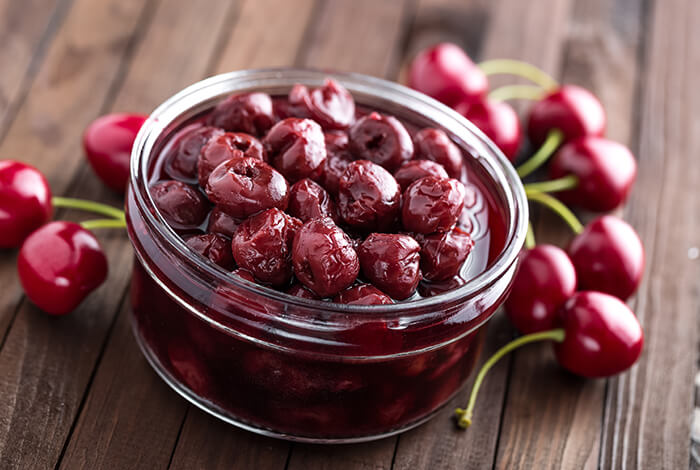 A jar of preserved cherries surrounded by fresh cherries.