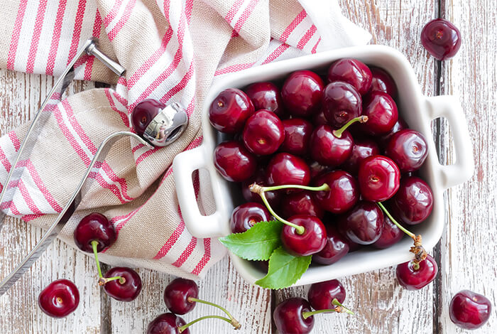 A bowl of fresh cherries placed on a wooden surface.