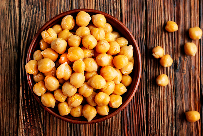 A wooden bowl brimming with cooked chickpeas.