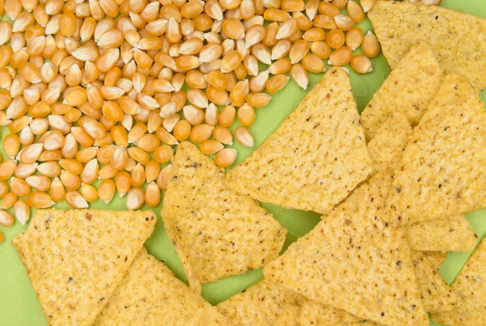 Tortilla chips and corn kernels placed side by side.